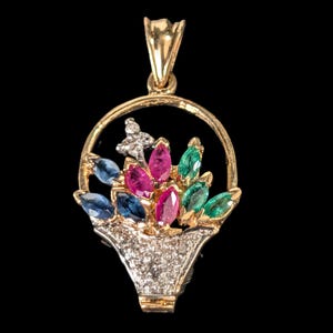 May include: A gold pendant shaped like a basket filled with flowers. The basket is encrusted with small white stones. The floral arrangement features marquise-cut gemstones in blue, pink, and green hues, set within a circular gold frame.