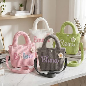 Könnte beinhalten: Vier Cord-Tragetaschen in Rosa, Weiß, Grau und Grün, jeweils mit Henkel und abnehmbarem Schultergurt. Die Taschen haben gestickte Namen und eine kleine Blume. Die Namen auf den Taschen sind Chloe, Emma, Bhma und Remi.