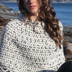 May include: A white and grey crochet poncho with a high neck and a textured pattern. The poncho is being worn by a person with long brown hair. The text "Whimsy Woolies" is visible in the bottom right corner of the image.