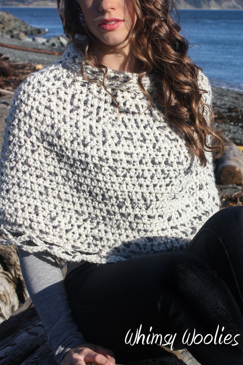 May include: A white and grey crochet poncho with a high neck and a textured pattern. The poncho is being worn by a person with long brown hair. The text "Whimsy Woolies" is visible in the bottom right corner of the image.