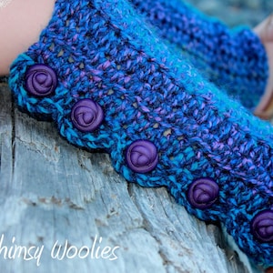 May include: Purple and blue crocheted leg warmers with purple buttons. The leg warmers are on a wooden surface.
