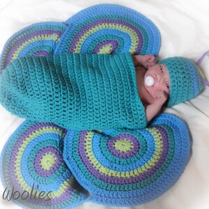 May include: A baby wearing a blue and purple crocheted butterfly costume with a pacifier in their mouth.