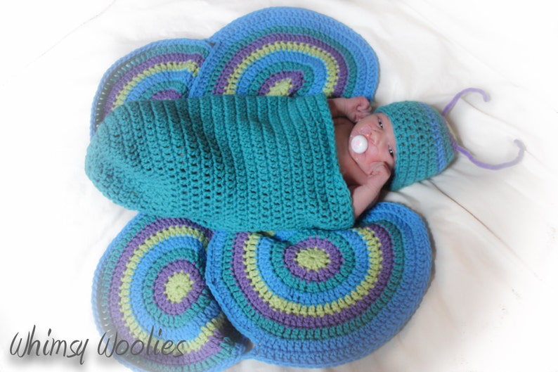 May include: A baby wearing a blue and purple crocheted butterfly costume with a pacifier in their mouth.