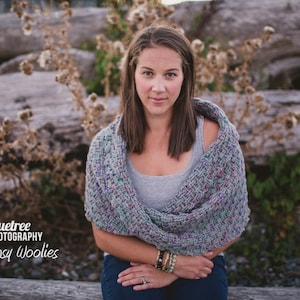 Peut inclure: Une écharpe col en tricot épais présentant un motif de fil moucheté multicolore dans des tons de gris, bleu et violet. L'accessoire texturé est drapé sur les épaules, mettant en valeur une construction tissée épaisse avec des boucles.