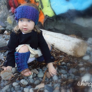 May include: A young girl wearing a purple and blue crocheted hat with a black jacket and matching leg warmers. The girl is sitting on a rock with a blurred background of a colorful wall.