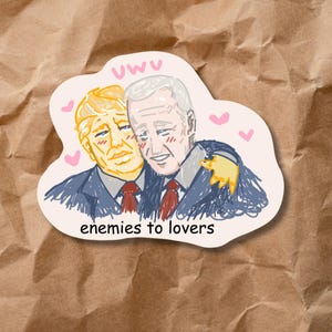 May include: A sticker featuring a cartoon illustration of two men embracing, with the text "enemies to lovers" below. The sticker has a light pink border, with the word "uwu" at the top.