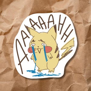 May include: A sticker featuring a cartoon Pikachu with tears streaming down its face. The word "AAAAHH" is written around the character. The Pikachu is yellow with red cheeks and a lightning bolt tail.