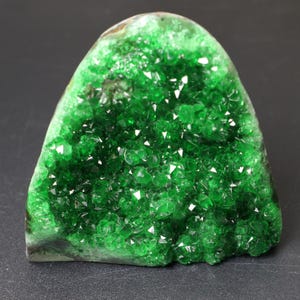 May include: A vibrant green crystal cluster, showcasing a multitude of sparkling, geometric formations. The natural stone has a rounded, irregular shape, with a rich, emerald hue. The surface is covered in small, reflective facets, creating a dazzling display of light and color.