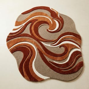 May include: A unique, abstract rug with a wavy design. The rug features a blend of warm colors, including shades of brown, orange, and white, creating a textured, artistic appearance. The rug's shape is irregular, adding to its distinctive appeal.