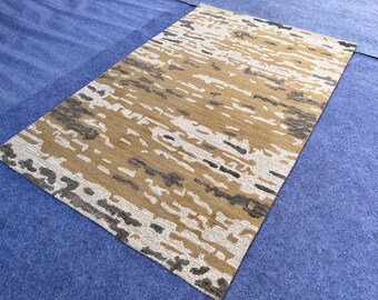 May include: A rectangular area rug featuring an abstract pattern with horizontal bands of ochre, charcoal gray, and cream white. The design consists of irregular, textured shapes that create a layered, organic appearance across the entire surface.