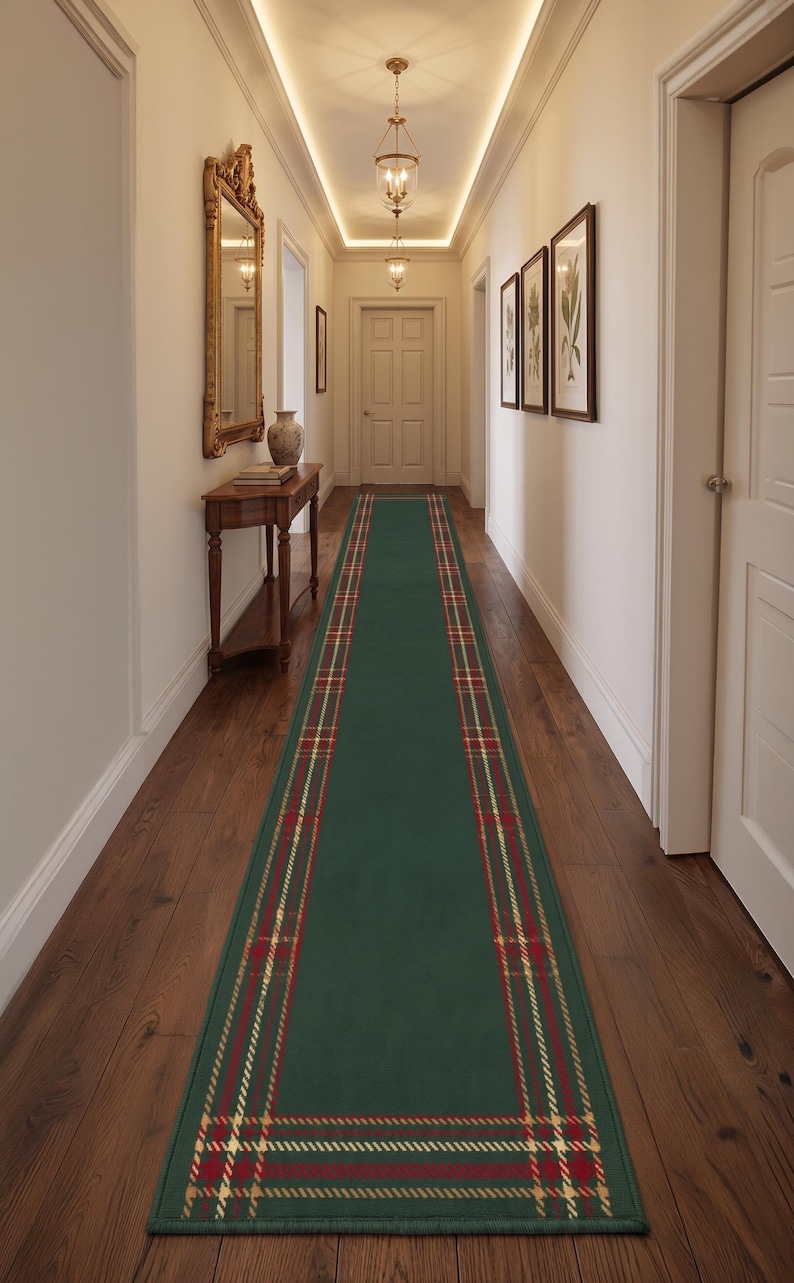 May include: A long rectangular runner rug featuring a solid dark green center panel framed by a decorative border with a red, gold, and white plaid pattern. The rug is positioned lengthwise along the center of a wooden floor in a hallway.