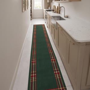 May include: A long rectangular runner rug featuring a solid dark green center panel framed by a decorative border. The border consists of a red and gold plaid pattern with thin intersecting lines, creating a classic tartan-inspired design.