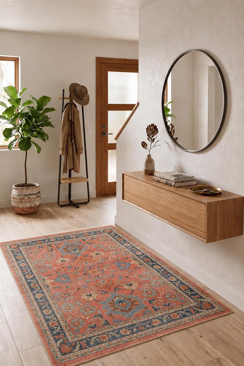 Pu&ograve; includere: Un interno di un corridoio con un tappeto color corallo con bordo blu navy. Sono visibili un attaccapanni, uno specchio e una consolle in legno. Una pianta in vaso e una porta in legno completano la scena.