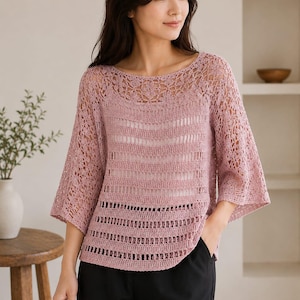 Puede incluir: Una blusa de ganchillo en color rosa empolvado con un amplio escote barco, mangas tres cuartos y un complejo patrón floral calado en el canesú. La prenda presenta bandas horizontales de tejido intrincado y una textura ligera y semitransparente.