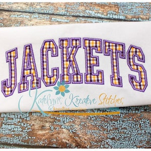 May include: White fabric with the word "JACKETS" in large, purple-outlined letters. The letters have a plaid pattern in yellow, orange, and black. The text "Katelyn's Kreative Stitches" is below the word "JACKETS".