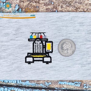 May include: Embroidered patch featuring a stylized sewing machine design with black, yellow, and white details, and a quarter coin for size comparison. The machine has a yellow screen and a rack of colorful spools.