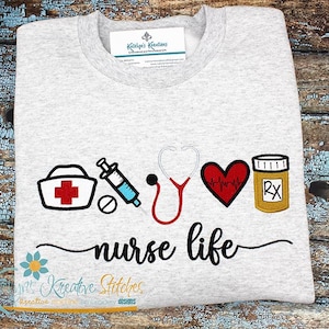 May include: A gray t-shirt with an embroidered design of a nurse's cap, syringe, stethoscope, heart with a heartbeat line, and a pill bottle with "RX" on it. The text "nurse life" is embroidered below the design.