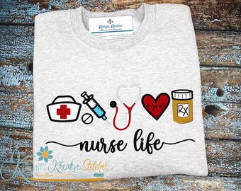 May include: A gray t-shirt with an embroidered design of a nurse's cap, syringe, stethoscope, heart with a heartbeat line, and a pill bottle with "RX" on it. The text "nurse life" is embroidered below the design.