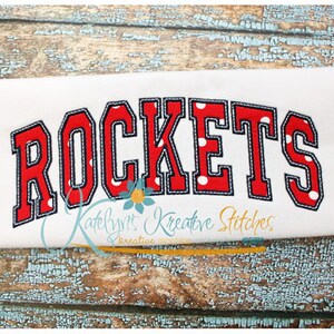 May include: Red and blue applique with white polka dots that reads "ROCKETS" on a white fabric background.