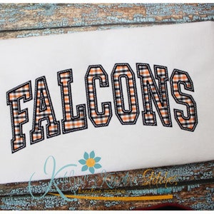 Könnte beinhalten: Weißes T-Shirt mit dem Wort "FALCONS" in schwarzen umrandeten Buchstaben mit einem schwarz-orangenen Karomuster.