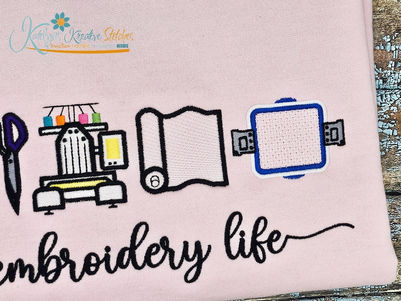 K&ouml;nnte beinhalten: Rosa Stoff mit gestickten Symbolen: Schere, N&auml;hmaschine, Stoffrolle und Stickrahmen. Die Worte "embroidery life" sind darunter in Schreibschrift geschrieben. Ein Logo mit Text und einer Blume befindet sich oben links.