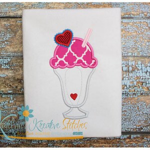May include: Embroidered design of a pink and white ice cream sundae with a red heart on top and a pink and white straw. The design is on a white fabric background.