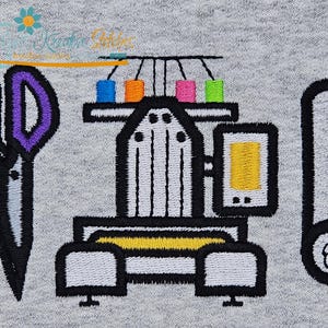 May include: Embroidered design featuring sewing tools and equipment. Includes scissors with purple handles, a sewing machine with colorful thread spools, and a roll of fabric. The design is on a gray background.