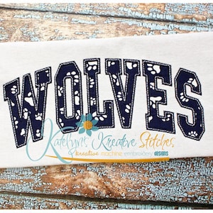 May include: Embroidered design of the word "WOLVES" in navy blue with white paw prints inside the letters. The design is on a white fabric background.