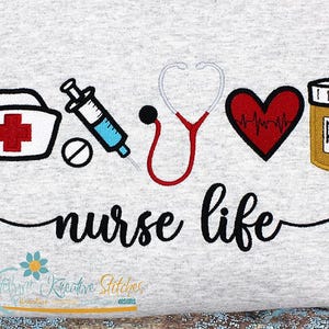 May include: A gray t-shirt with an embroidered design featuring a nurse's cap, a syringe, a stethoscope, a heart with a heartbeat line, a pill bottle with an RX symbol, and the text "nurse life".