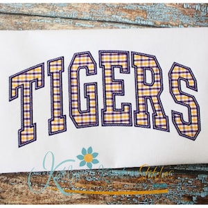 May include: White t-shirt with the word "TIGERS" embroidered in a yellow and purple plaid pattern.