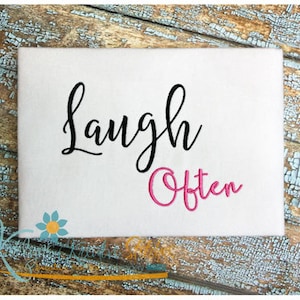 May include: White fabric with black cursive text that says "Laugh" and pink cursive text that says "Often".