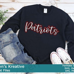 Könnte beinhalten: Ein schwarzer Pullover mit dem Wort "Patriots" in rot-weißer Schrift. Der Pullover ist gefaltet und liegt auf einer Holzoberfläche mit einem Paar weißen Turnschuhen und einer blauen Jeans.