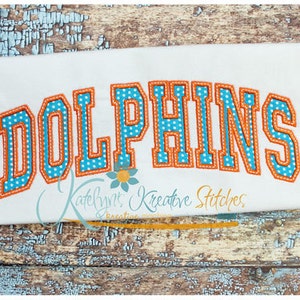 May include: White t-shirt with a blue and orange embroidered "DOLPHINS" in a varsity style font.