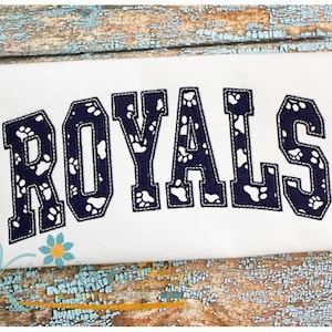 May include: White fabric with the word "ROYALS" in navy blue outlined in white. The letters are filled with a pattern of white paw prints on a navy blue background.