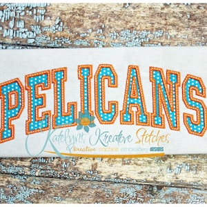 May include: Embroidered design of the word "PELICANS" in orange and blue with white polka dots. The design is on a white fabric background.