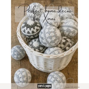 May include: A white wicker basket filled with gray and white crocheted spheres. The spheres have a granny square design. The text "Perfect home decor for Xmas" is at the top of the image. The spheres are on a wooden surface.