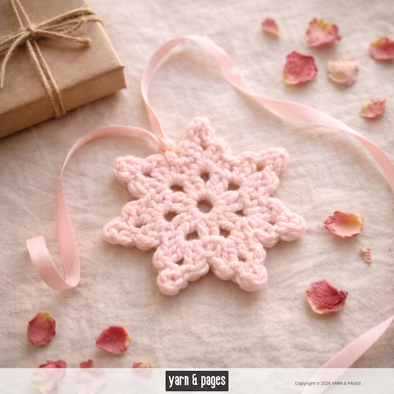 May include: A handmade, light pink crochet snowflake ornament with a delicate ribbon. The snowflake is surrounded by scattered rose petals and a wrapped gift box. The image has a soft, romantic aesthetic.