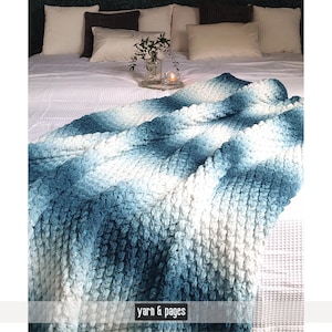 May include: A textured, blue and white blanket draped over a bed. The blanket has a gradient effect, transitioning from dark blue to white. The text "yarn & pages" is at the bottom of the image. Pillows and decorative items are in the background.