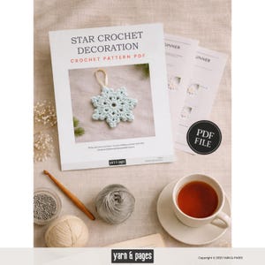 May include: A crochet pattern PDF titled "Star Crochet Decoration" featuring a light blue crocheted star ornament. The image includes yarn, a crochet hook, and a cup of tea, suggesting a crafting theme. The PDF file is labeled with a "PDF FILE" sticker.