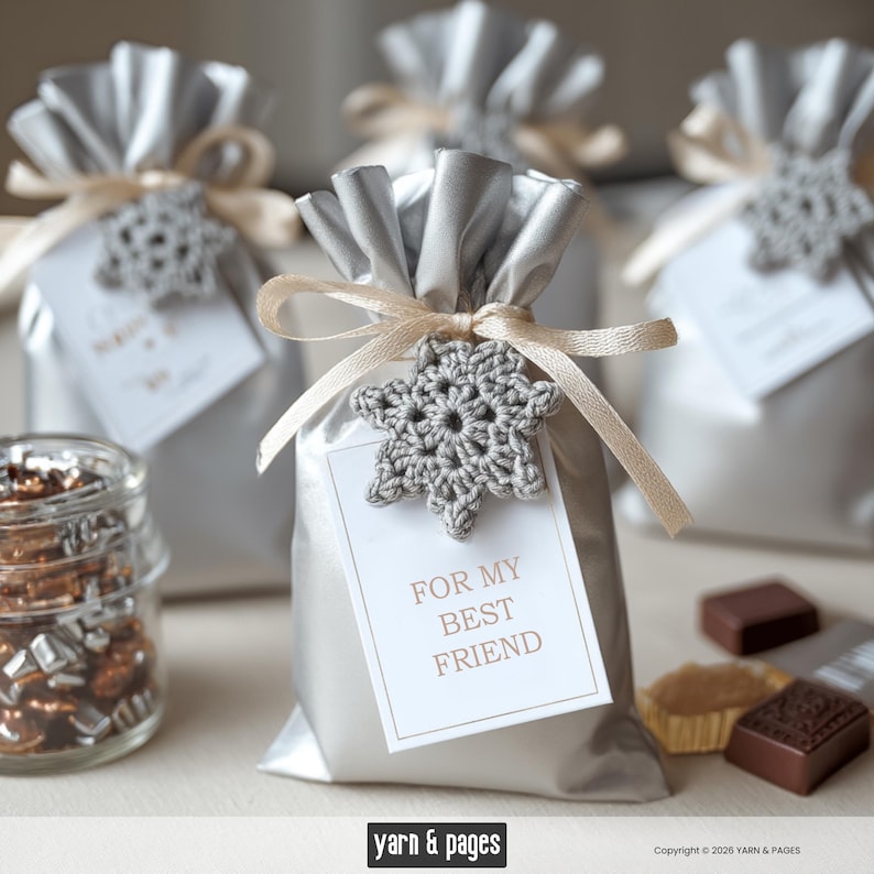 May include: Silver gift bags tied with beige ribbons and adorned with crocheted snowflake ornaments. Each bag has a tag that reads "FOR MY BEST FRIEND". A jar of treats and chocolates are in the foreground. The image is from Yarn & Pages.