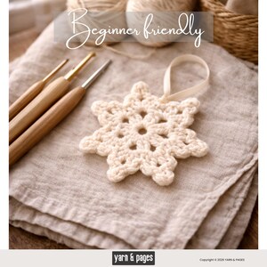May include: A cream-colored, crocheted snowflake ornament with a ribbon loop, resting on a folded linen cloth. The image also shows three wooden crochet hooks and the text "Beginner friendly".