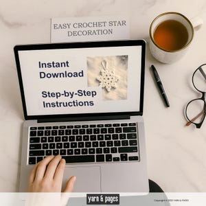 May include: A laptop displays "Instant Download Step-by-Step Instructions" for a crochet star decoration. A crocheted star is shown on the screen. A cup of tea, a pen, and glasses are on the table. The text "Easy Crochet Star Decoration" is on a paper.