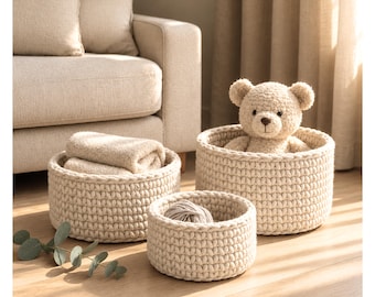 May include: Three round, cream-colored crocheted baskets with a thick, textured knit pattern. One basket holds a folded beige cloth, another contains a plush teddy bear, and the third holds a ball of yarn. Text reads: yarn & pages.