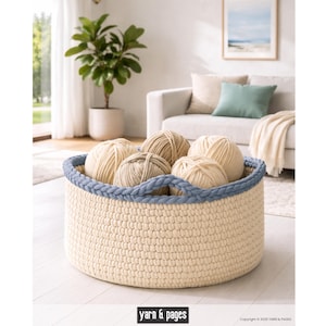 Puede incluir: Una cesta redonda de ganchillo color crema con un borde trenzado azul, llena de varias madejas de hilo en varios tonos neutros. La cesta est&aacute; sobre una superficie clara. El texto "yarn & pages" es visible en la parte inferior.