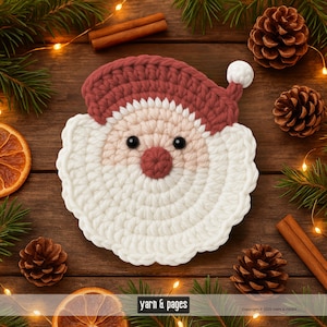 May include: A handmade crochet Santa Claus coaster with a red hat and nose, white beard, and black eyes. The coaster is surrounded by pine cones, cinnamon sticks, and dried orange slices on a wooden surface. The text "yarn & pages" is visible.