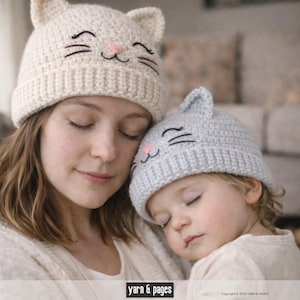 May include: Two knitted cat hats, one cream-colored and one light gray, each with embroidered black whiskers and a pink nose. The hats have cat ears on top. The hats are worn by a person and a child.