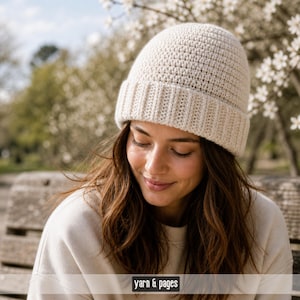Könnte beinhalten: Eine cremefarbene Häkelmütze mit geripptem Rand. Die Mütze ist aus einem weichen, strukturierten Garn gefertigt. Der Text "yarn & pages" ist unten im Bild zu sehen. Die Mütze ist ein stilvolles Accessoire für kühleres Wetter.