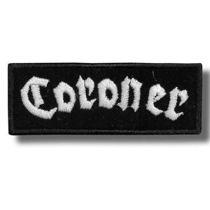 Könnte beinhalten: Ein rechteckiger, schwarzer Aufnäher mit dem Wort "Coroner" in weißer, gotischer Schrift gestickt. Der Aufnäher hat einen schwarzen Rand und ist wahrscheinlich zum Aufnähen auf Kleidung oder Accessoires gedacht.