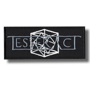 Puede incluir: Parche bordado negro con la palabra "ESPERA" en hilo gris, con un diseño geométrico en el centro. El parche es rectangular y tiene un fondo negro.