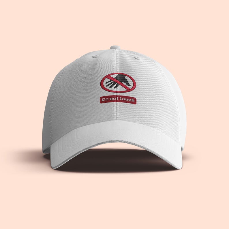 Peut inclure: Casquette de baseball blanche avec une visi&egrave;re incurv&eacute;e. Le chapeau pr&eacute;sente un motif brod&eacute; d'une main dans un cercle rouge barr&eacute;, avec les mots "Do not touch" en dessous.